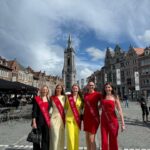 Les Miss Tournai 2025 sur le podium de la Grand-Place, célébrant la fête nationale avec un ciel belge typique.